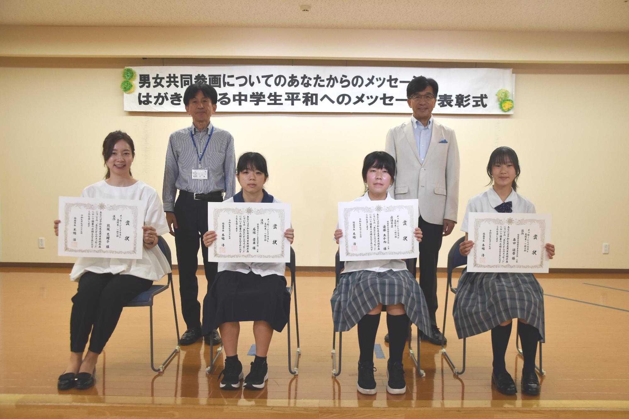 イラストとメッセージ高校生一般の部の入賞者が座り賞状を見せながら笑顔で記念撮影をしている写真
