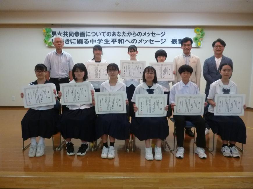 関係者3名と1列目の椅子に6名の中学生、中央に3名の中学生が賞状を見せながら笑顔で記念撮影をしている写真