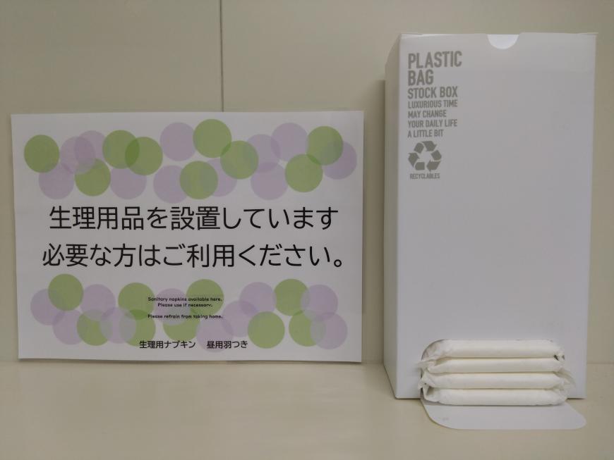 箱の中に生理用品がいれられ、横には「生理用品を設置しています 必要な方はご利用ください。と案内が書かれた実際におかれている様子を写した写真