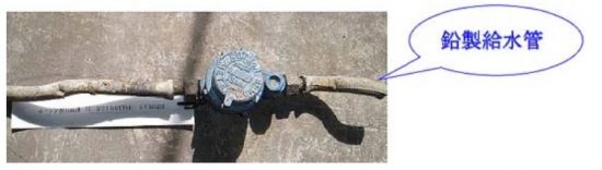 コンクリートの地面に設置された、青色の水道メーターと、それに接続されている鉛製給水管の写真