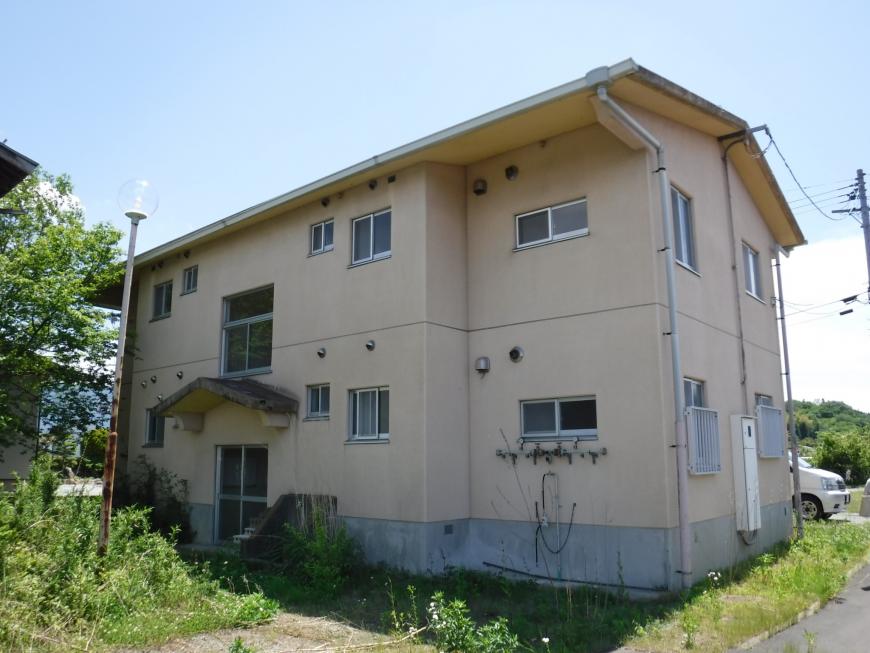 2階建てのベージュ色の外壁の入り口側を写した飯野町教職員住宅の写真