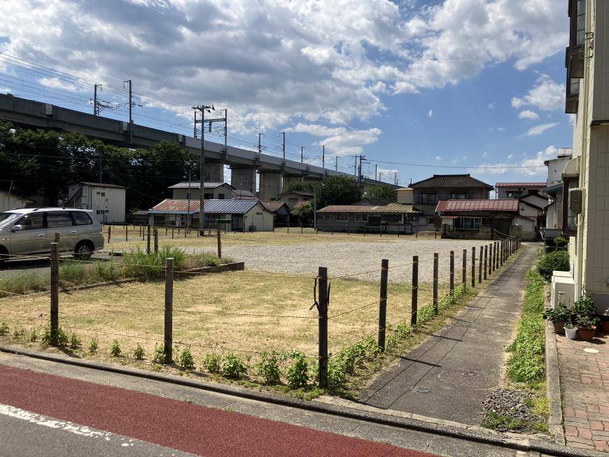 電車の高架近くにある杭とロープで囲まれた更地の写真