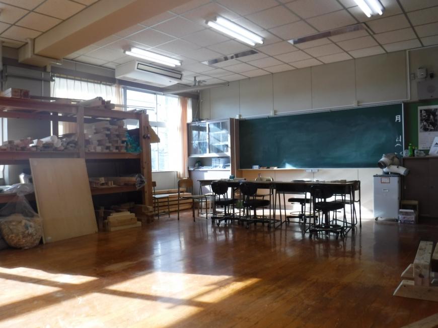 前方に黒板があり左側には材料置き場の棚があり、机が並べられた木造建築科の実習室の写真