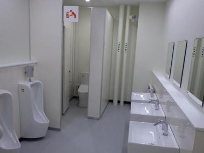 白を基調とした左側に男性用便器、奥の個室に洋式トイレがあり、右側に鏡がある手洗い場が設けられた男性用トイレ内の写真
