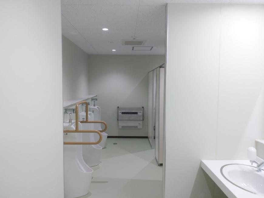 白を基調とした左側に男性用便器、右側に個室が設置されたトイレ内の写真
