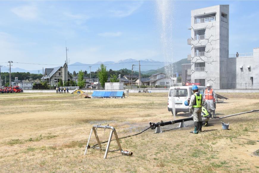 水が吹き上げている水道管の応急復旧訓練を行っている作業者の写真
