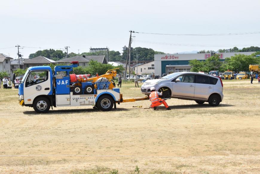 作業員の方がシルバーの車をレッカー車につなげようとしている写真