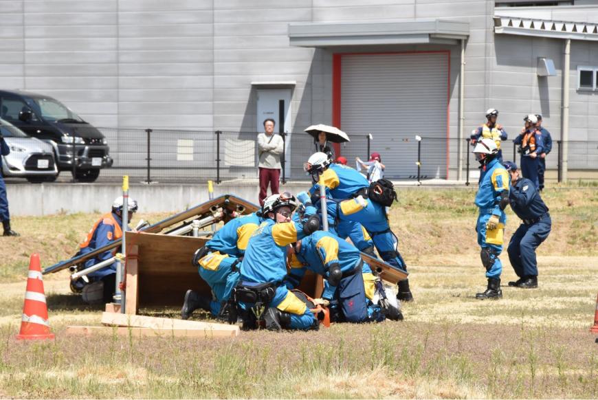 黄色と水色の作業着を着た方々が、倒壊した建物を模したセットを使って救出救助訓練を行っている写真