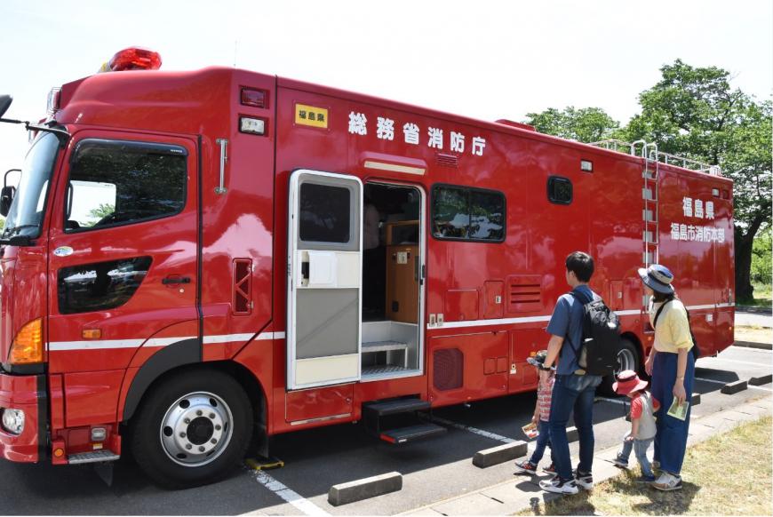 赤い車体に白で「総務省消防庁」と書かれた大きな消防車両を見学しているお父さん、お母さん子供2人の写真
