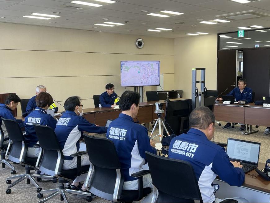 ロの字型に長机が設置された席に関係者達が座り、災害対策本部設置訓練が行われている写真