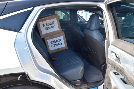 乗用車の後部座席に「支援物資（福島市）」と書かれた段ボールが2箱乗っている写真