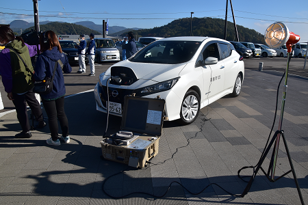 電気自動車のフロント部分にケーブルをつなぎ、充電を行っている様子の写真