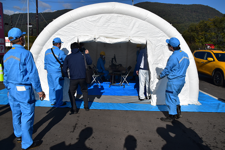 半円形のテントが立てられ、関係者の方々が中の様子を伺っており、中には中央に置かれた机と椅子に関係者の方が座っている電力本部の様子の写真