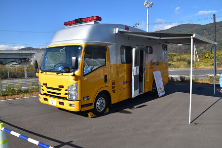 黄色い大型の車でルーフの上に赤色灯がついており、左横のドア開き、日よけが設置されている車を写した写真