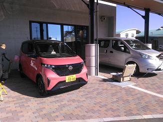 ピンク色の軽自動車とシルバーの普通車2台が停まっており、充電器からケーブルを伸ばし充電している様子の写真