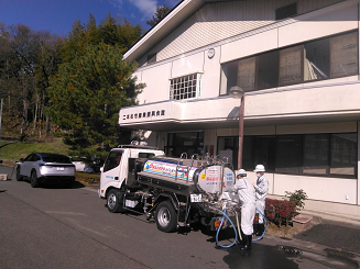 建物の前に給水車が停まっており、関係者2名が作業を行っている様子の写真