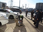 電気自動車2台と機械が電源ケーブルでつながれ、電源供給する訓練が行われている様子の写真