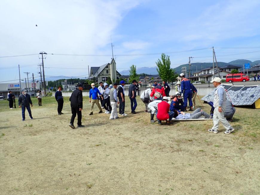 広場の地面に置かれた担架に乗っている方の周りに人が集まっている写真