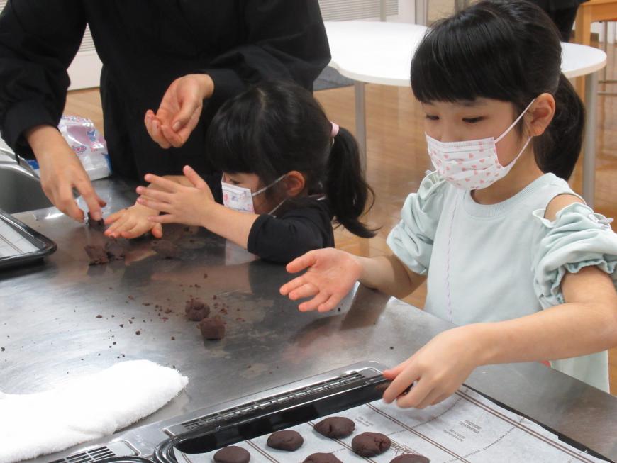 1人の女の子がクッキー生地を丸めて形を作り、隣の女の子がクッキーの生地を並べている写真