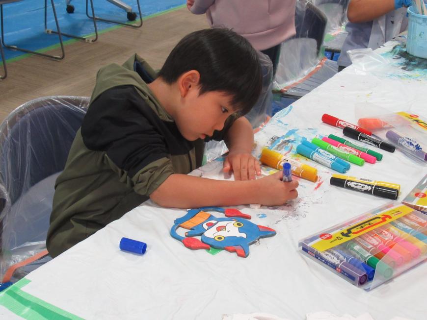机の上で男の子が青色のマッキーで絵を描いている写真