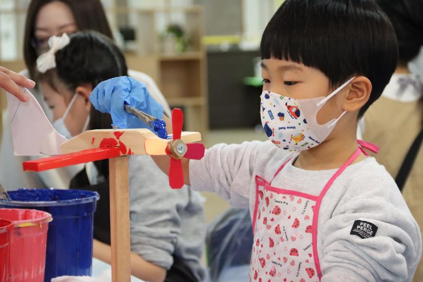 マスク姿の男の子が木材でできた風車にペンキで色付けをしている写真