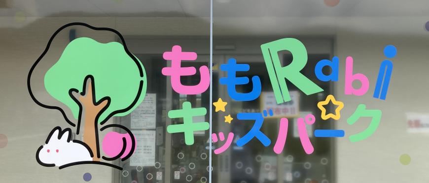 透明のガラス窓に一本の木の下に桃とウサギがいるイラストと、カラフルな色で「ももRabiキッズパーク」と書かれた写真