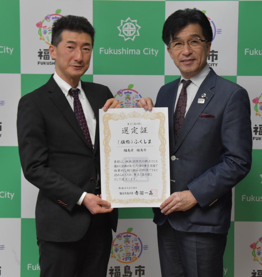 福島市のバックパネルの前で、佐藤克英国土交通省東北地方整備局長と市長が一緒に選定証を持ち並んでいる写真