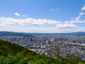 青空の下、山に囲まれた民家などが広がっている福島市の市街地の写真