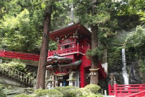 岩から流れ出る不動滝の左側に建つ、朱色で塗られた奥の院の写真