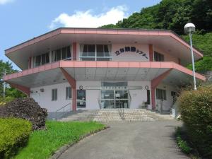 坂道を上がった先にあるピンク色の縁に白壁のUFOふれあい館の建物外観の写真