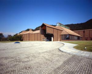 信夫山の麓の広大な敷地に建つ、茶色の外壁の県立美術館の建物外観の写真