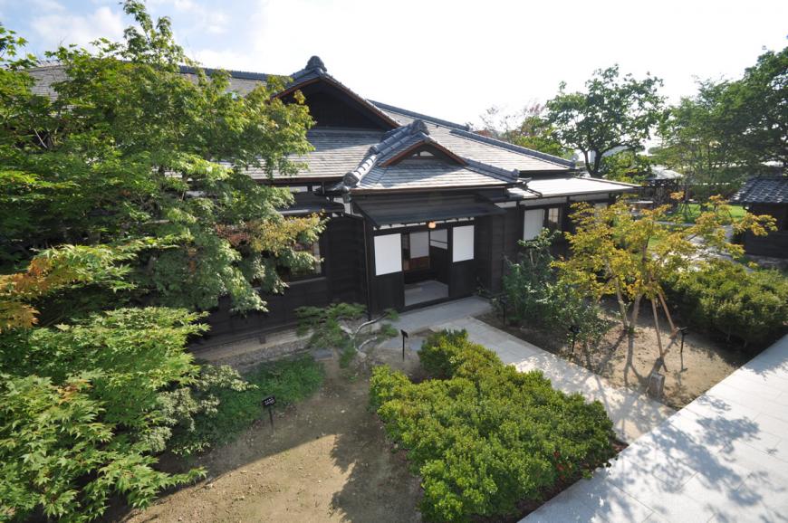 植木が植栽された中央に石畳の通りがあり、その先にある近代和風住宅の旧堀切邸主屋の建物入り口の写真