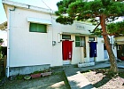 一本の松の木が立っている前に、青が男湯と赤が女湯の暖簾が設置された、白壁の八幡の湯の建物外観の写真