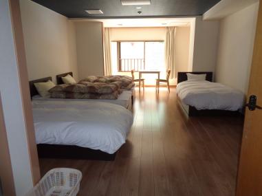 フローリング床の部屋に4つのベッドが備え付けられた宿泊室の写真