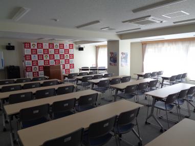 3脚ずつ椅子がセットされた長机が2列ずつ並んでいる会議室の写真