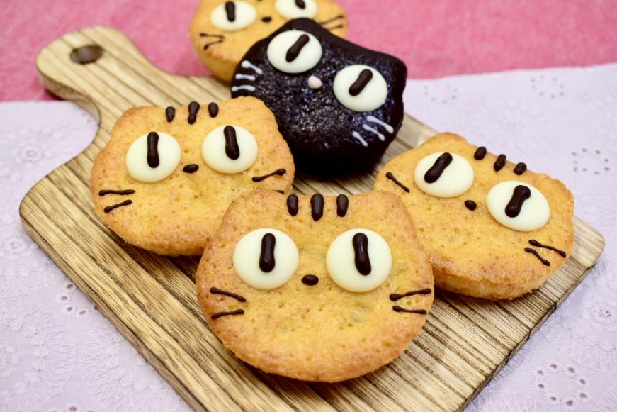 木製トレイの上に、猫の顔の形をした4個のお菓子が置かれた茶トラのポンムの写真