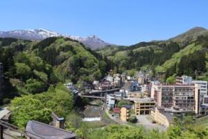 遠くの山の上には雪が残り、山に囲まれた土湯温泉町を展望広場から撮影した写真