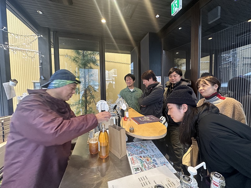 参加者の前で蔵元がお酒を注ぎながら話をしている蔵元ツアーの様子の写真