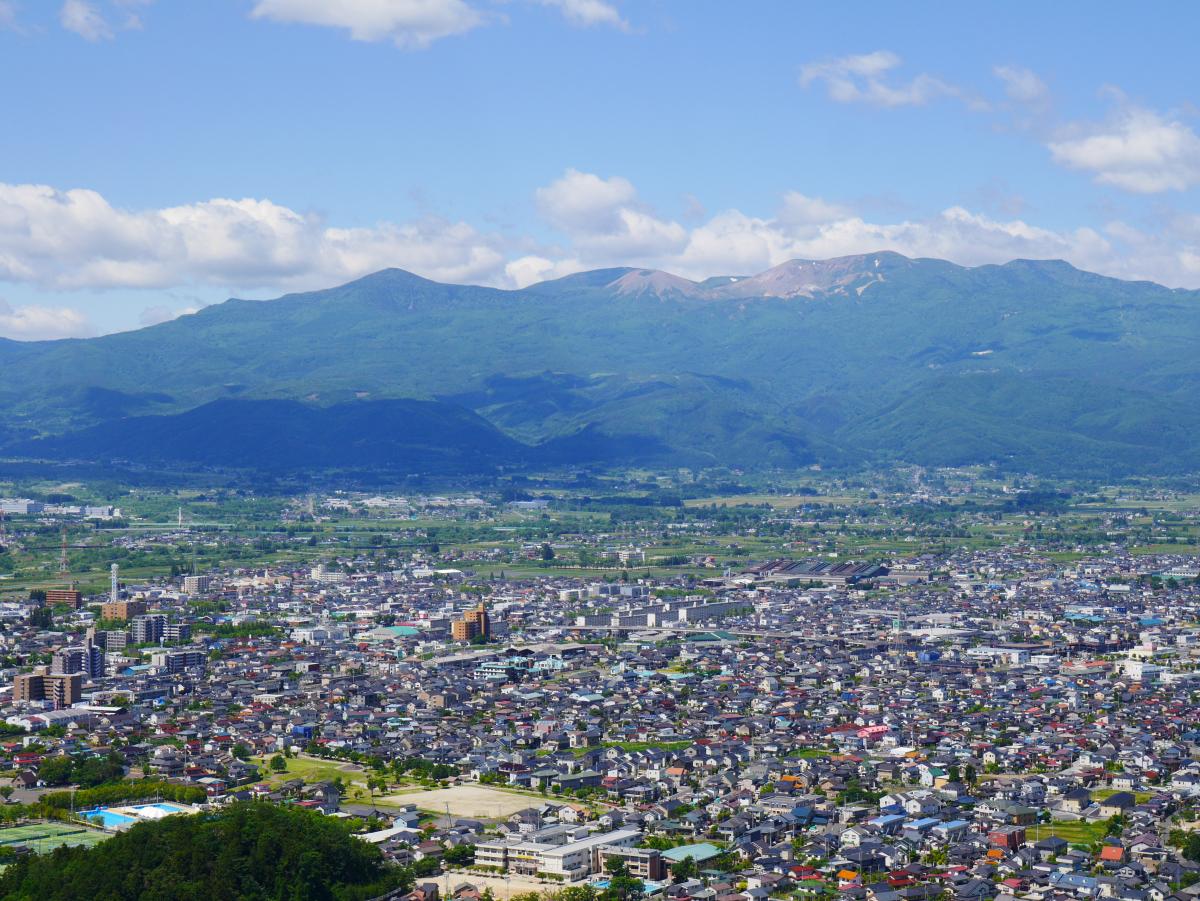 民家などが建ち並ぶ市街地と、吾妻連峰を高台から撮影した写真