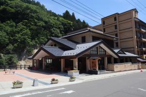 山の麓に建ち、入り口の建物が二重屋根造りでベージュ色の外壁の中之湯の建物外観の写真