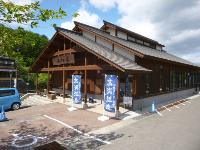 2本ののぼり旗が設置された入り口の建物が二重屋根造りで、茶色の外壁の高湯温泉の建物外観の写真