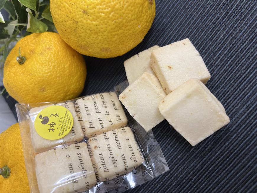 英語の文字が書かれた透明の袋に四角形の4個入りのお菓子が入り、外に袋から出したお菓子が重ねて置かれた柚子のショートブレッドの写真