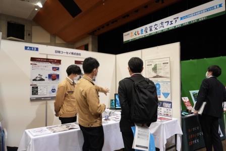 黄土色のジャンパーを着た男性スタッフから説明を受けている男性の写真