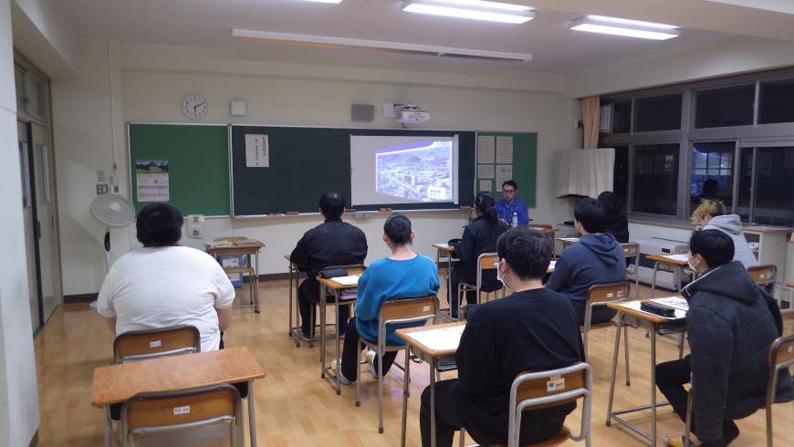 資料が映し出された黒板の右側に立つ男性担当者の話を、自席に座った生徒たちが熱心に聞いている写真