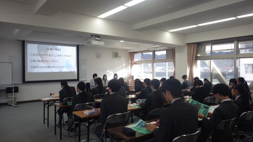 お願い事項と表示されたスクリーンの右側に座った担当者の話を、長机の席に2名ずつ座った高校生が熱心に聞いている様子を左後方から撮影した写真