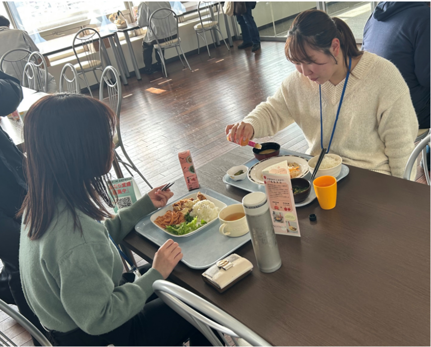 テーブルに向かい合って座った2名の女性が食事に「ももスコ」をかけている様子の写真
