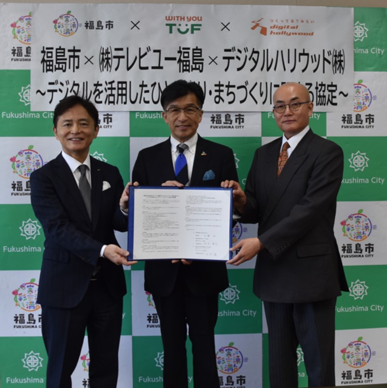 福島市のバックパネルの前で市長を中央に仲尾代表取締役社長と吉村代表取締役社長兼CEOが横一列に並び、一緒に協定書を持っている写真