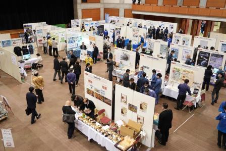 ブースごとに資料がパネルに展示され、製品が並んでいる広い会場の全景写真