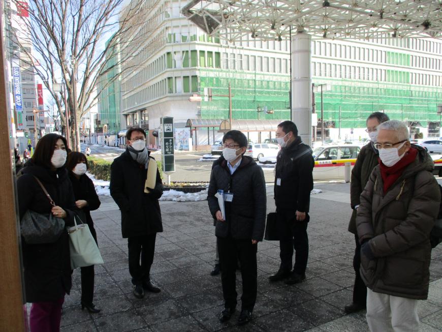 道の端に雪が寄せられた駅前に複数の参加者が立っている写真