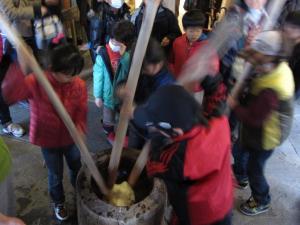 長い棒で臼の中の餅をついている子供たちの写真